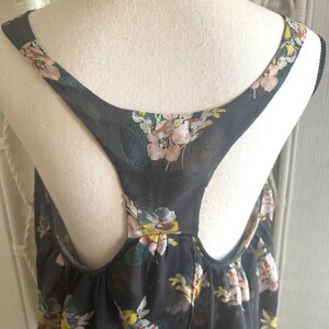 K&ouml;nnte beinhalten: Schwarzes Tanktop mit einem Blumenmuster in Rosa, Gelb und Gr&uuml;n. Das Oberteil hat ein Racerback-Design und besteht aus einem transparenten Stoff. Der Blumendruck ist &uuml;ber den Stoff verstreut.