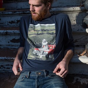 Peut inclure: Un homme portant une chemise à manches longues bleu marine avec un imprimé graphique d'une femme assise dans une voiture rouge dans un champ. La chemise a un col blanc et un imprimé blanc sur le devant. L'homme porte un jean bleu.