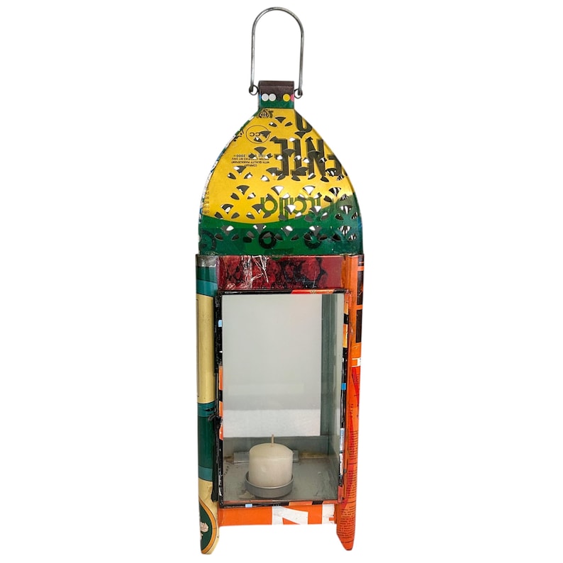 May include: A colorful metal lantern with a handle. The lantern has a yellow, green, and orange design with cut-out patterns. A white candle sits inside the glass-paneled interior. The lantern is made of recycled materials.