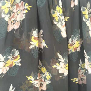 K&ouml;nnte beinhalten: Nahaufnahme eines dunkelgrauen, durchsichtigen Oberteils mit floralem Muster. Die Blumen sind in Gelb-, Rosa- und Wei&szlig;t&ouml;nen gehalten, mit gr&uuml;nen Akzenten. Das Oberteil hat einen runden Ausschnitt und einen flie&szlig;enden, leichten Stoff.