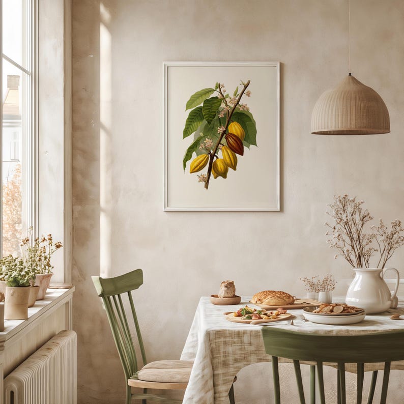 May include: A framed botanical print featuring a detailed illustration of a cacao branch with green leaves, yellow and brown pods, and delicate white flowers. The print is displayed in a bright, airy dining room setting with a green chair and a table set for a meal.