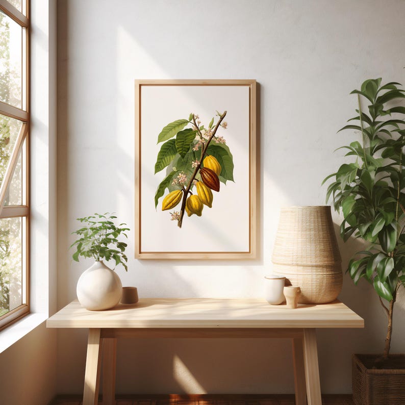 May include: A framed botanical print featuring a detailed illustration of a cacao branch with green leaves, yellow and brown cacao pods, and delicate white flowers. The artwork is displayed on a light wooden table, enhancing the natural theme.
