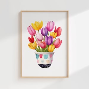 May include: A watercolour painting of a bouquet of tulips in a decorative pot. The tulips are in shades of yellow, pink, purple, and red. The pot is white with a blue, red, and yellow pattern and a black dotted base. The artwork is framed in a light brown wooden frame.