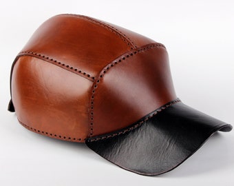 May include: A brown leather baseball cap with a black leather brim. The cap has stitching details around the seams.