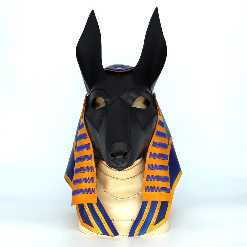 May include: A black leather anubis mask with blue and orange trim. The mask has a pointed snout and large ears. The mask is on a white background.