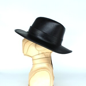 May include: A black leather fedora hat with a wide brim. The hat is sitting on a tan leather mannequin head.