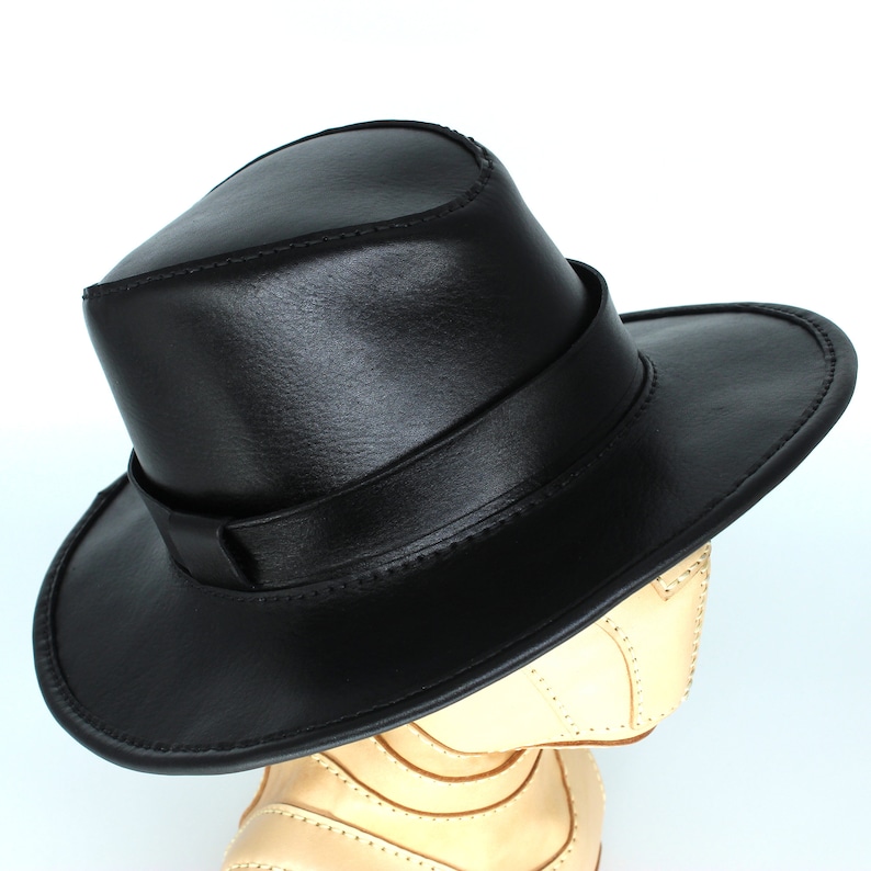 May include: A black leather fedora hat with a wide brim and a stitched band around the crown.