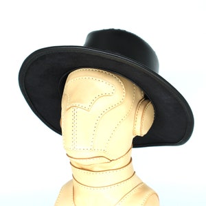 May include: A black leather hat with a wide brim and a tan leather face mask. The hat is sitting on a mannequin head.