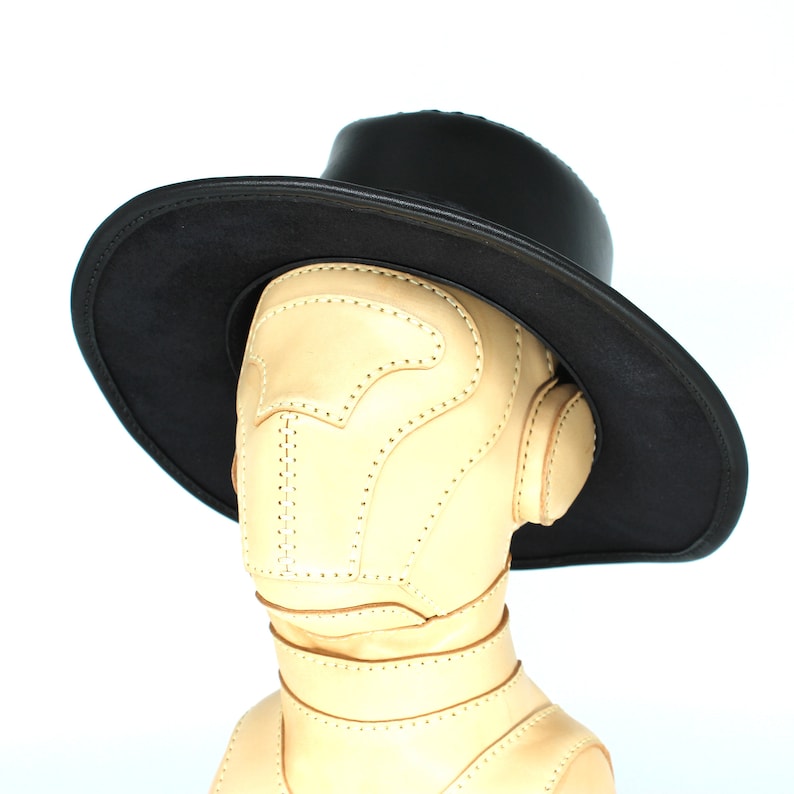May include: A black leather hat with a wide brim and a tan leather face mask. The hat is sitting on a mannequin head.