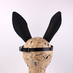 Peut inclure: Un serre-t&ecirc;te oreilles de lapin noir avec une bande en cuir noir. Le serre-t&ecirc;te est sur une t&ecirc;te de mannequin recouverte de papier journal.