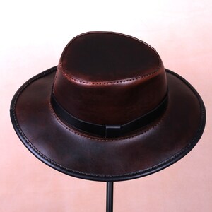 May include: A brown leather fedora hat with a black band. The hat has a wide brim and a classic design.