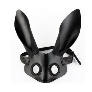 Peut inclure: Un masque de lapin en cuir noir avec de grandes oreilles et des trous pour les yeux. Le masque est dot&eacute; d'une sangle qui passe autour de la t&ecirc;te.