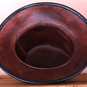 May include: A brown leather hat with a black leather trim around the brim. The hat is turned inside out, showing the brown leather lining.