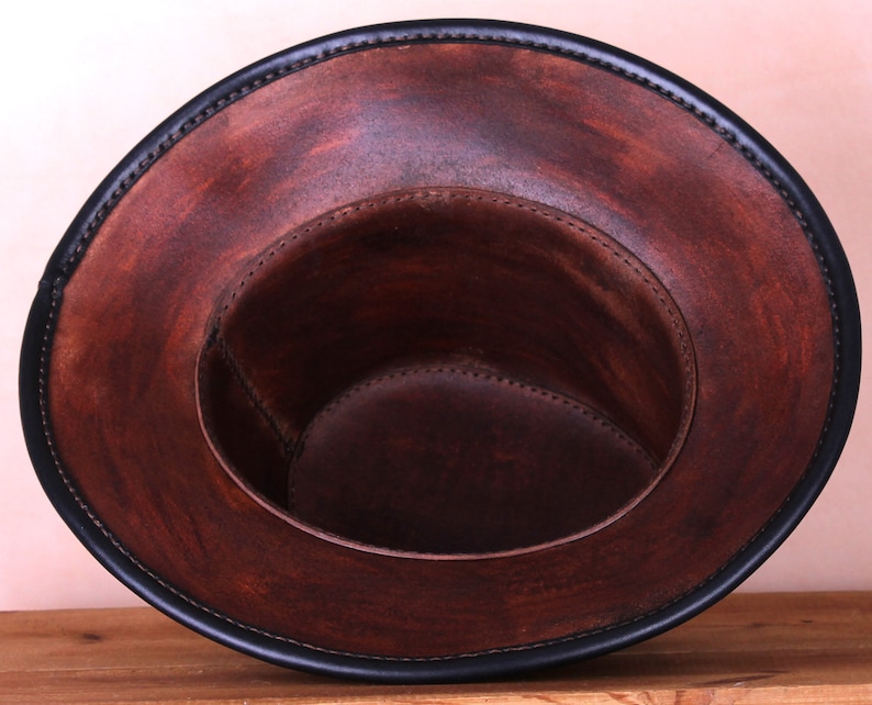 May include: A brown leather hat with a black leather trim around the brim. The hat is turned inside out, showing the brown leather lining.