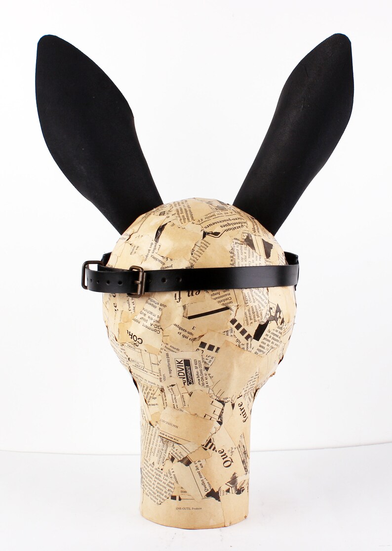 Peut inclure: Un masque de lapin noir avec de longues oreilles et une sangle en cuir noir. Le masque est en papier m&acirc;ch&eacute; et recouvert de coupures de journaux.
