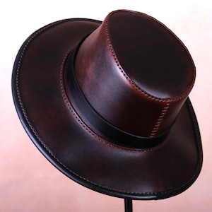 May include: A brown leather fedora hat with a black band. The hat has a wide brim and a tall crown.