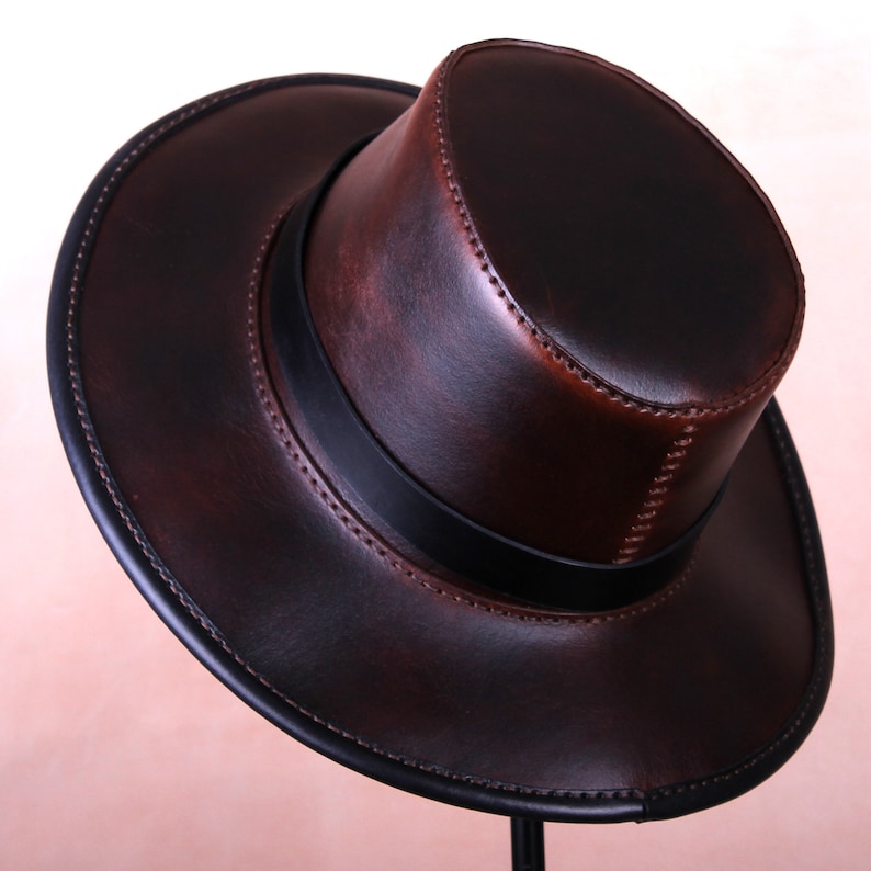 May include: A brown leather fedora hat with a black band. The hat has a wide brim and a tall crown.