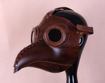Könnte beinhalten: Eine braune Ledermaske eines Pestarztes mit einem langen Schnabel und zwei runden Augenlöchern. Die Maske befindet sich auf einem schwarzen Mannequin-Kopf.