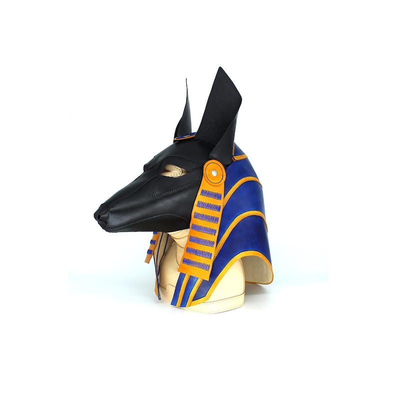 May include: A black leather Anubis mask with blue and gold accents. The mask is on a mannequin head and is a side view.