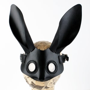 Peut inclure: Un masque de lapin en cuir noir avec de grandes oreilles et des trous ronds pour les yeux. Le masque est dot&eacute; d'une sangle qui passe autour de la t&ecirc;te.