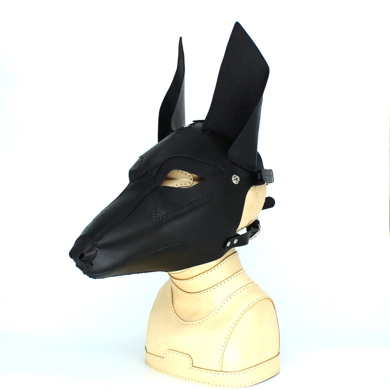 May include: Black leather dog mask with pointed ears and a strap. The mask is on a mannequin head.
