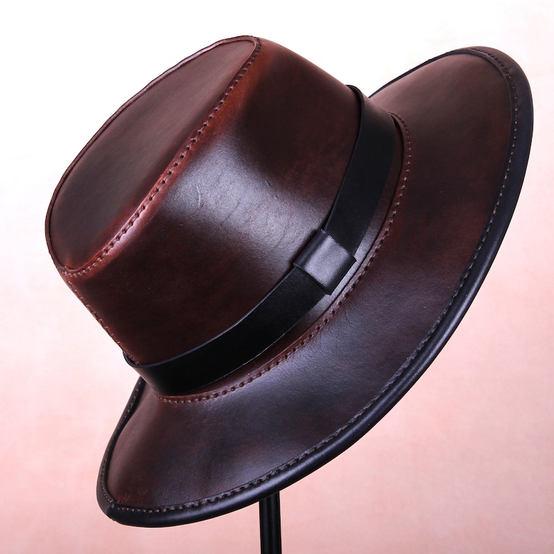 May include: A brown leather fedora hat with a black leather band. The hat has a wide brim and a stitched edge.