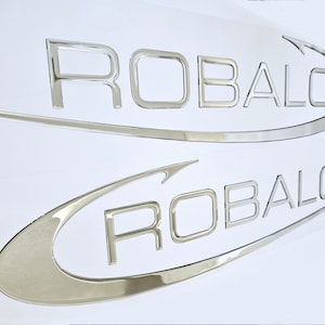 May include: Two silver metallic decals with the word "ROBALO" in a curved font. The decals are on a white background.