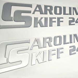 May include: Two silver-colored vinyl decals with the text "CAROLINA SKIFF 24DLX".