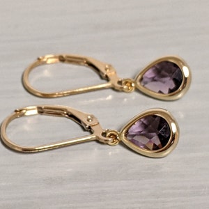 Könnte beinhalten: Ein Paar goldene Ohrringe mit tropfenförmigen Amethyststeinen.