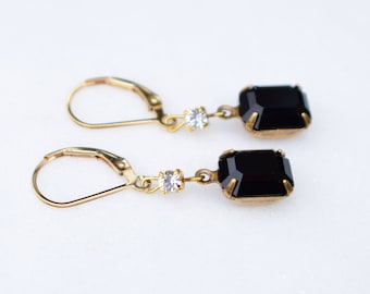 May include: A pair of gold earrings with black square-shaped stones and small clear rhinestones.