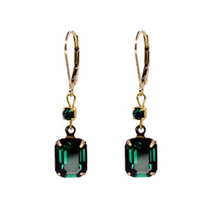 May include: A pair of gold-tone leverback earrings featuring a small round dark green crystal at the top and a larger rectangular emerald-cut dark green crystal suspended below, held in place by four metal prongs on each stone setting.