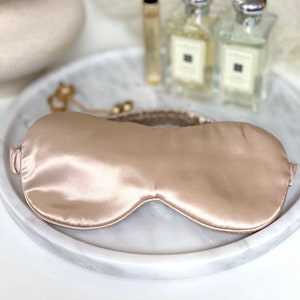 Op de afbeelding: Een lichtbeige satijnen slaapmasker met een dun elastisch bandje.