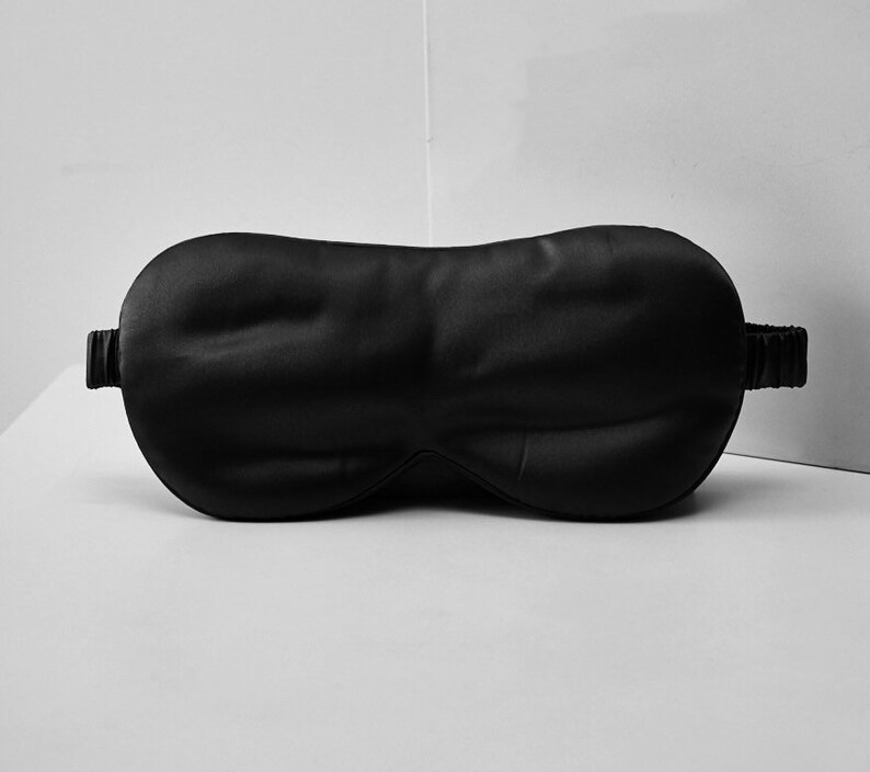 Op de afbeelding: Een zwart satijnen slaapmasker met een elastisch bandje.