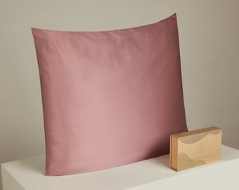 Op de afbeelding: Een stoffig roze kussensloop met een subtiele glans. De kussensloop is gemaakt van een zachte, gladde stof. De kussensloop ligt op een wit oppervlak met een klein bruin doosje waarop "Liz Liz Boutique" staat.