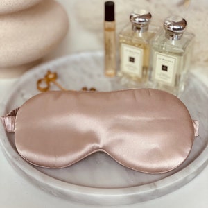 Op de afbeelding: Een lichtroze zijden slaapmasker op een wit marmeren dienblad.