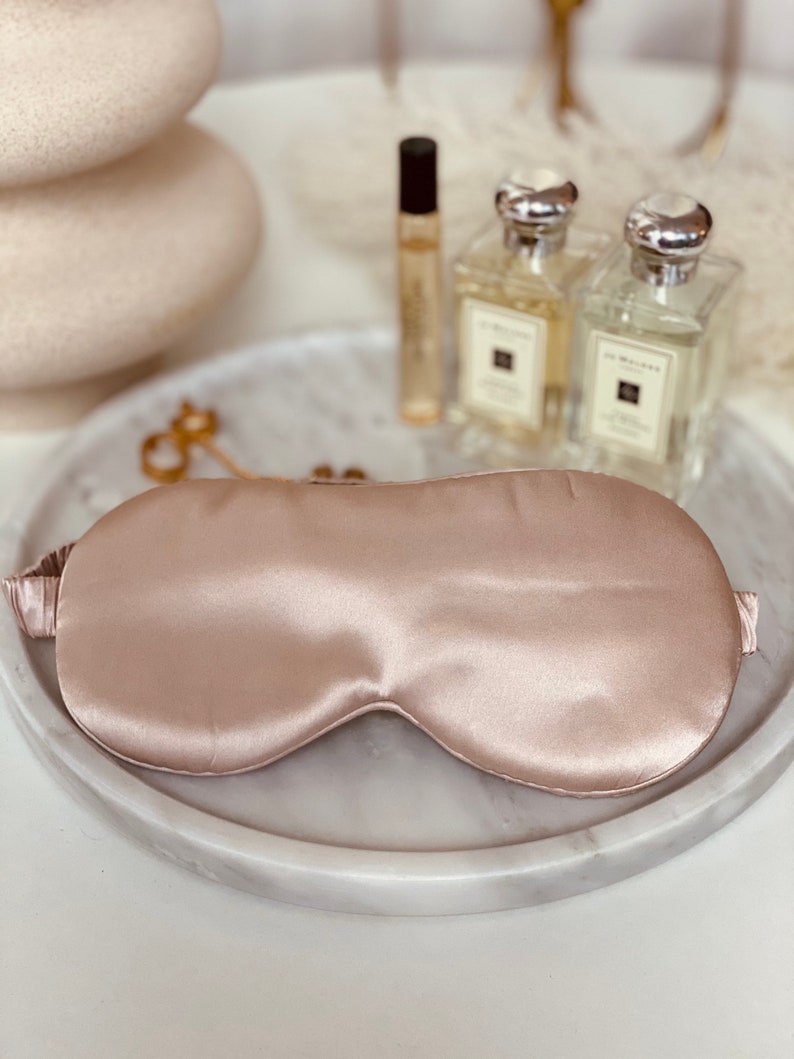 Op de afbeelding: Een lichtroze zijden slaapmasker op een wit marmeren dienblad.