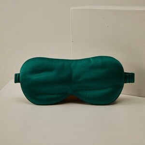 Op de afbeelding: Een donkergroen satijnen slaapmasker met een elastisch band.
