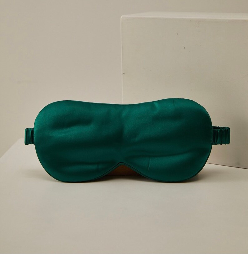 Op de afbeelding: Een donkergroen satijnen slaapmasker met een elastisch band.