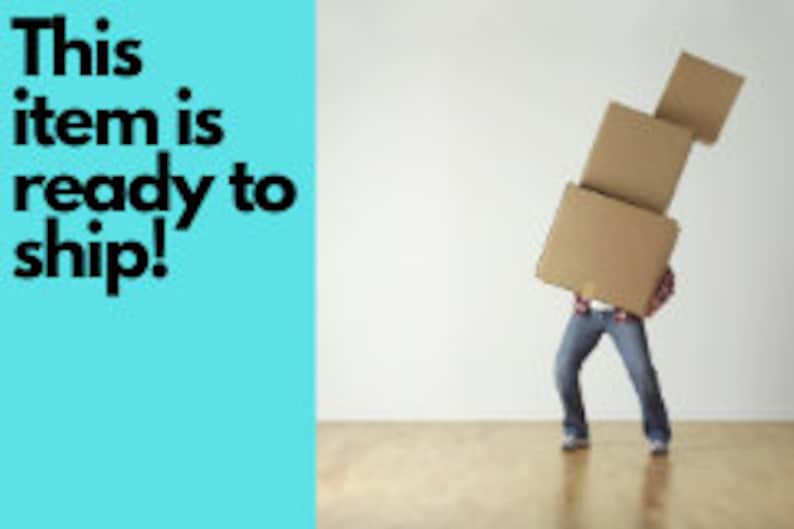 May include: A person carrying three stacked cardboard boxes. The boxes are brown and rectangular. The person is wearing blue jeans and a plaid shirt. Text on the left says "This item is ready to ship!"