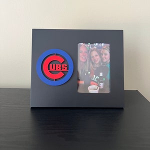May include: Black picture frame with a red and blue Chicago Cubs logo and a photo of three women inside.