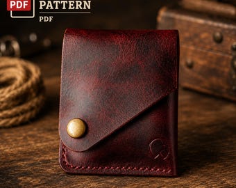 Puede incluir: Una cartera de cuero rojo oscuro con un cierre de solapa diagonal asegurado con un botón de presión de metal color latón. La cartera tiene costuras visibles a lo largo del borde inferior y un pequeño logotipo en relieve. El texto dice LEATHER PATTERN PDF.