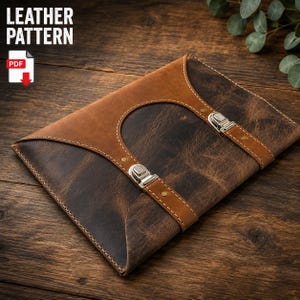 May include: A two-tone leather portfolio case featuring a dark brown distressed leather body and a lighter tan leather flap. The case includes two vertical leather straps secured with silver-toned metal buckles and visible stitching.