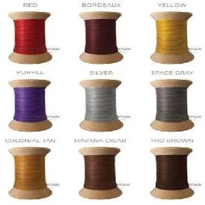 May include: Fifteen wooden spools of thread arranged in a grid, each labeled with its color name: orange, red, bordeaux, yellow, pea green, blue, purple, silver, space gray, white, beige, colonial tan, havana cigar, mid brown, and black.