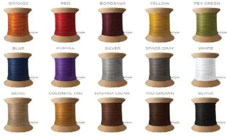 May include: Fifteen wooden spools of thread arranged in a grid, each labeled with its color name: orange, red, bordeaux, yellow, pea green, blue, purple, silver, space gray, white, beige, colonial tan, havana cigar, mid brown, and black.