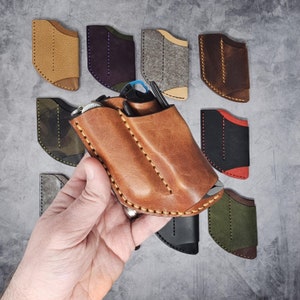 May include: A collection of nine leather pouches in various colors and styles, including brown, black, green, red, and camouflage. The pouches are designed to hold small items like knives, tools, or other accessories.