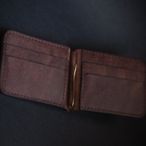 May include: A brown leather wallet with a money clip. The wallet has multiple card slots and a fold-over design.
