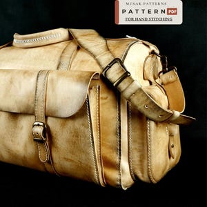 Puede incluir: Un bolso de viaje de cuero color canela con costuras blancas, un asa superior y una correa ajustable con hebillas de metal color bronce. El bolso cuenta con un bolsillo frontal con solapa y cierre de hebilla. El texto dice MUSAK PATTERNS PATTERN PDF FOR HAND STITCHING.