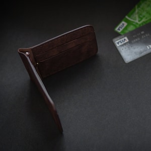 May include: A brown leather wallet is open and lying on a black surface. Two credit cards are visible in the background, one with the word "VISA" printed on it.