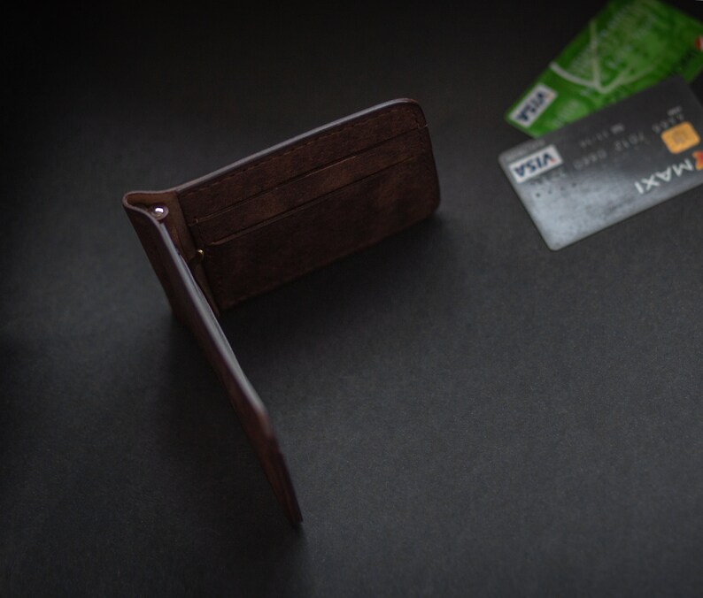 May include: A brown leather wallet is open and lying on a black surface. Two credit cards are visible in the background, one with the word "VISA" printed on it.