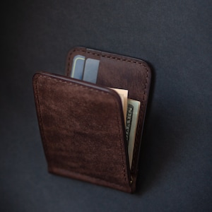 May include: A brown leather wallet with a money clip and a credit card slot. The wallet is closed and has a bill sticking out of the top.